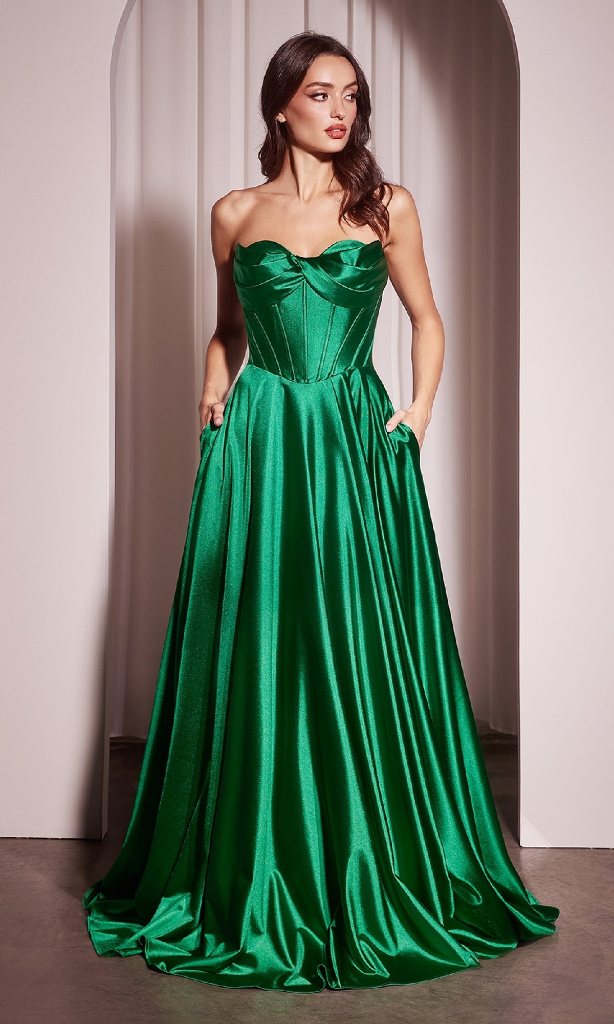 A woman stands in front of a white archway, looking to the side with one hand in her pocket, wearing the Ladivine CD378 Strapless Long A-Line Prom Dress featuring a corset-style bodice.